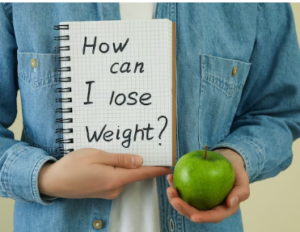 Person holding a green apple and a notebook with 'How can I lose weight?' written on it, suggesting intermittent fasting as a strategy.