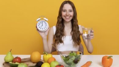 A woman holding a clock surrounded by food, illustrating intermittent fasting.